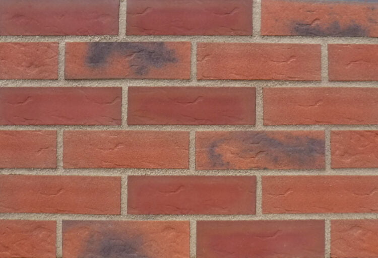 A panel of brick slips laid out in stagger bond. The bricks are a blend of red and black tones with a sanded, textured surface finish.
