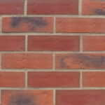 A panel of brick slips laid out in stagger bond. The bricks are a blend of red and black tones with a sanded, textured surface finish.